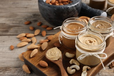 Photo of Tasty nut butters and raw nuts on wooden table