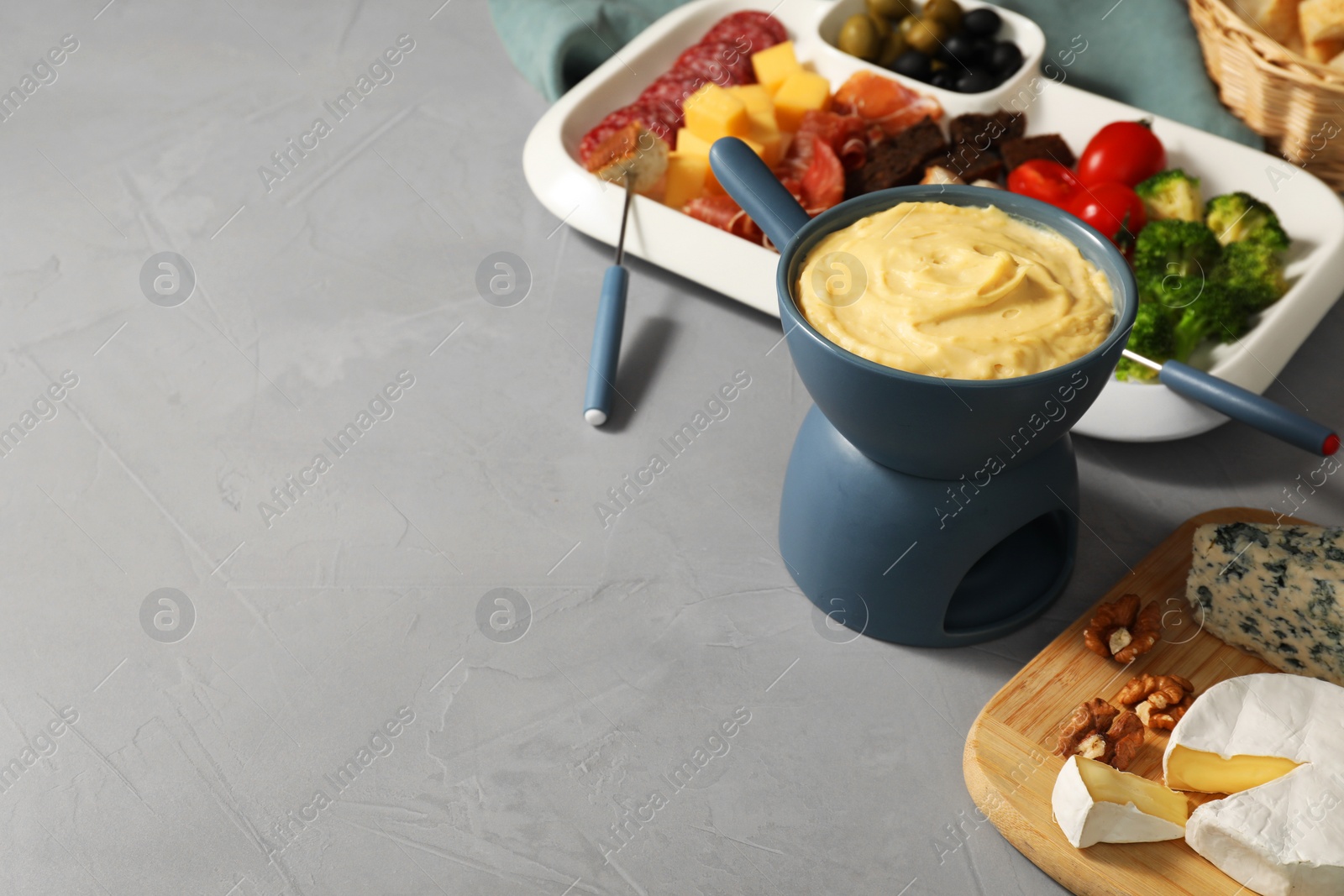 Photo of Fondue with tasty melted cheese, forks and different snacks on grey table, space for text