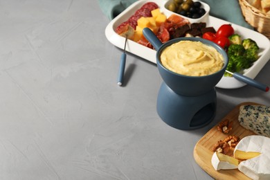 Fondue with tasty melted cheese, forks and different snacks on grey table, space for text