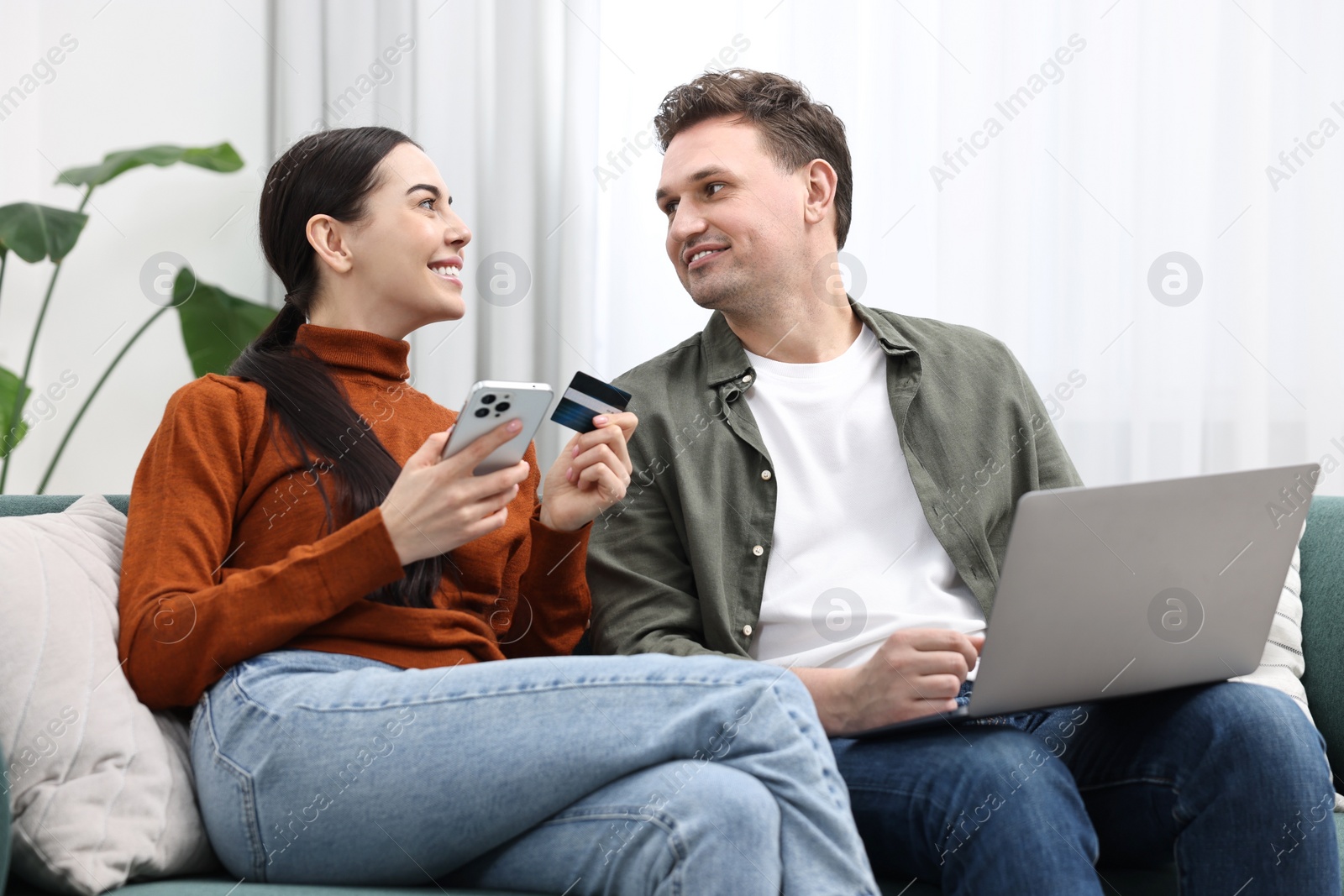 Photo of Happy couple with credit card and gadgets shopping online together at home