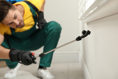 Photo of Pest control worker spraying insecticide on window sill at home, focus on device