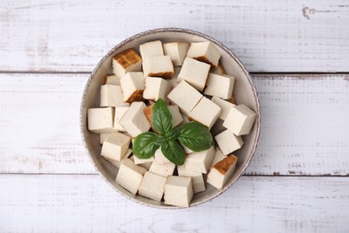 Photo of Bowl with delicious smoked tofu and basil on white wooden table, top view