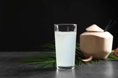 Glass with fresh coconut water on table against black background