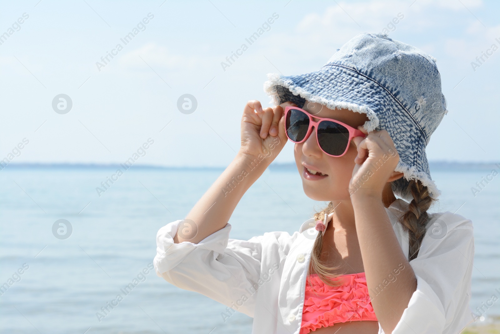 Photo of Little girl wearing sunglasses and hat at beach on sunny day. Space for text