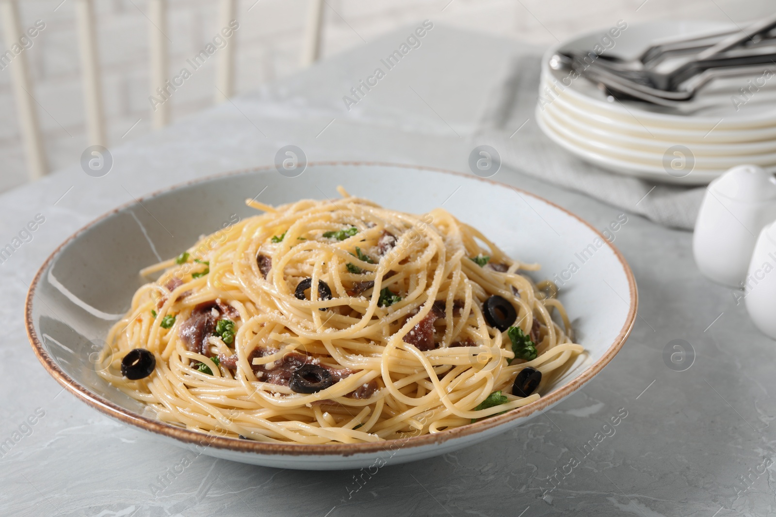 Photo of Delicious pasta with anchovies, olives and parmesan cheese served on grey marble table, closeup