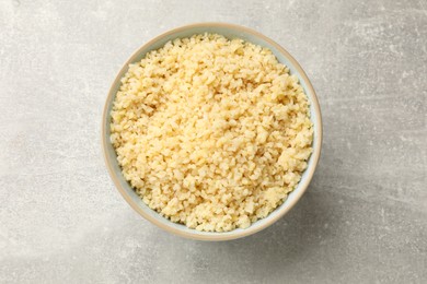 Delicious bulgur in bowl on light grey table, top view