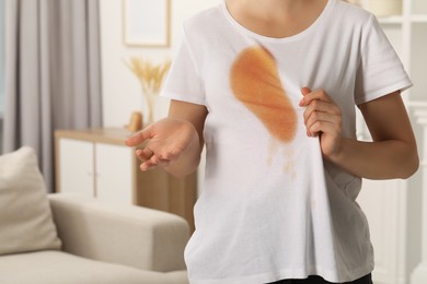 Woman showing stain from coffee on her shirt indoors, closeup. Space for text