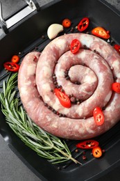 Photo of Pan with raw homemade sausage, chili pepper, garlic and rosemary on grey table, top view