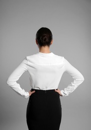 Young businesswoman in elegant suit on grey background, back view