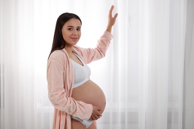 Photo of Beautiful pregnant woman in stylish comfortable underwear and robe indoors, space for text