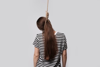 Woman with rope noose on neck against light grey background, back view