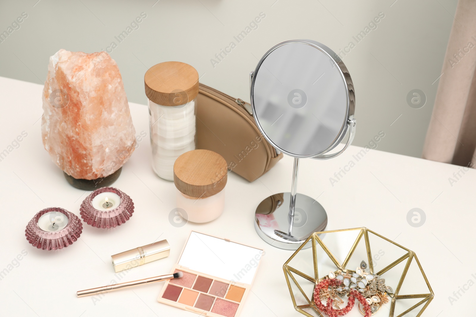 Photo of Dressing table with mirror, cosmetic products, jewelry and burning candles in makeup room