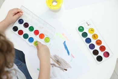 Photo of Little boy painting with brush and watercolor at white table, top view