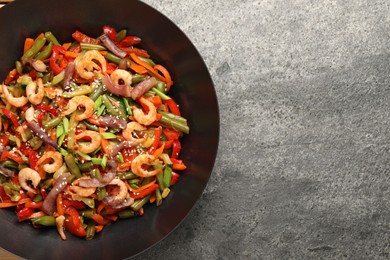 Photo of Shrimp stir fry with vegetables in wok on grey table, top view. Space for text