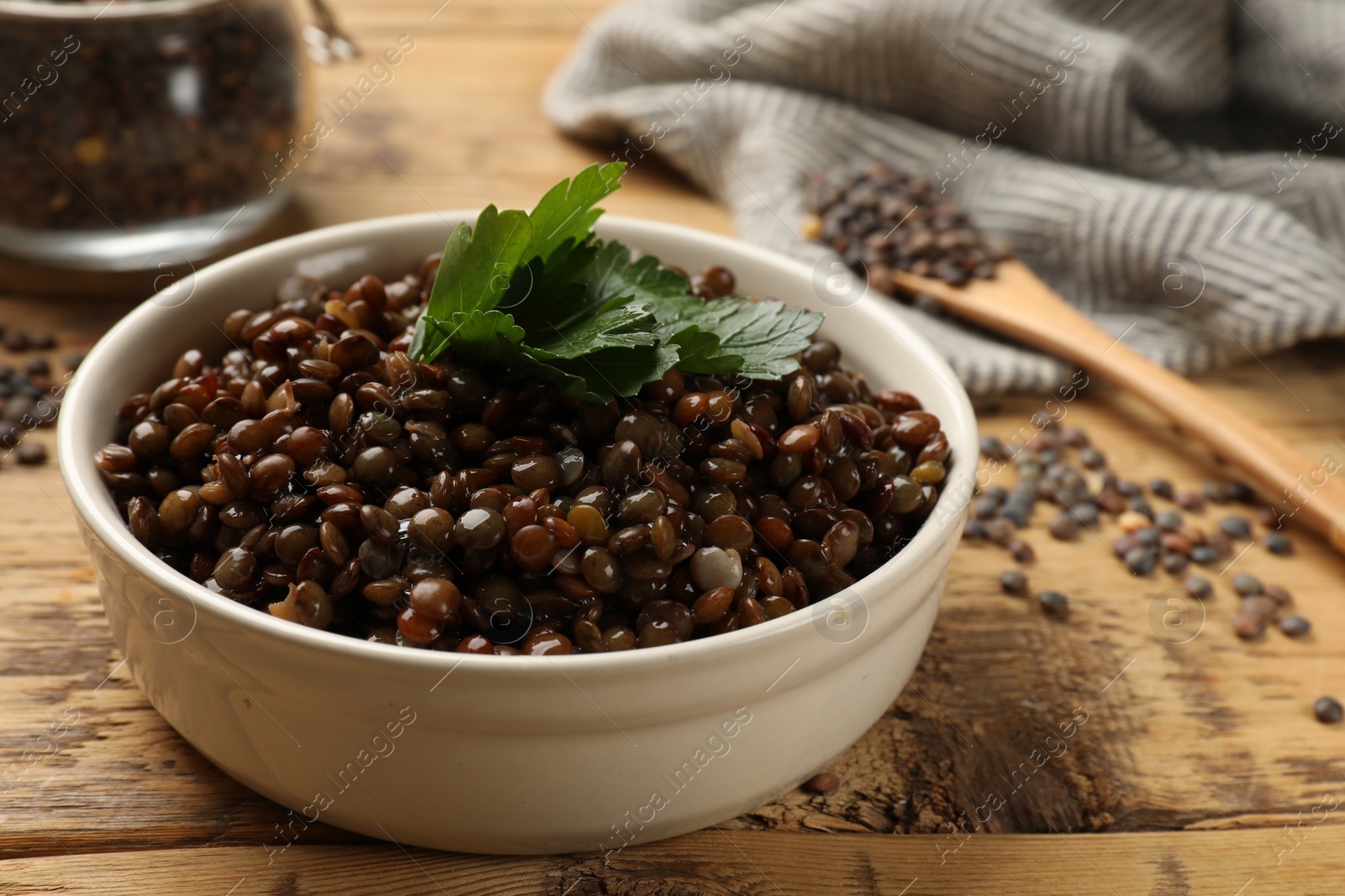 Photo of Delicious lentils with parsley in bowl on wooden table, closeup