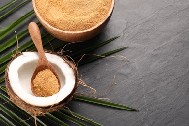 Photo of Spoon with coconut sugar, fruit, bowl and palm leaves on dark textured table, above view. Space for text