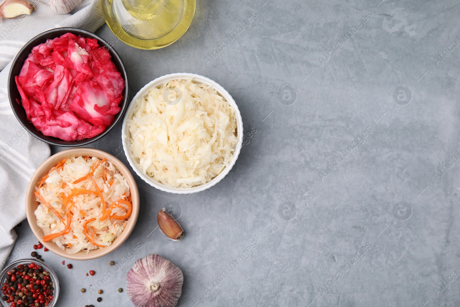 Photo of Delicious sauerkraut prepared according to different recipes and spices on gray table, flat lay. Space for text