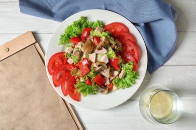 Photo of Plate with delicious fresh salad and menu on table, top view