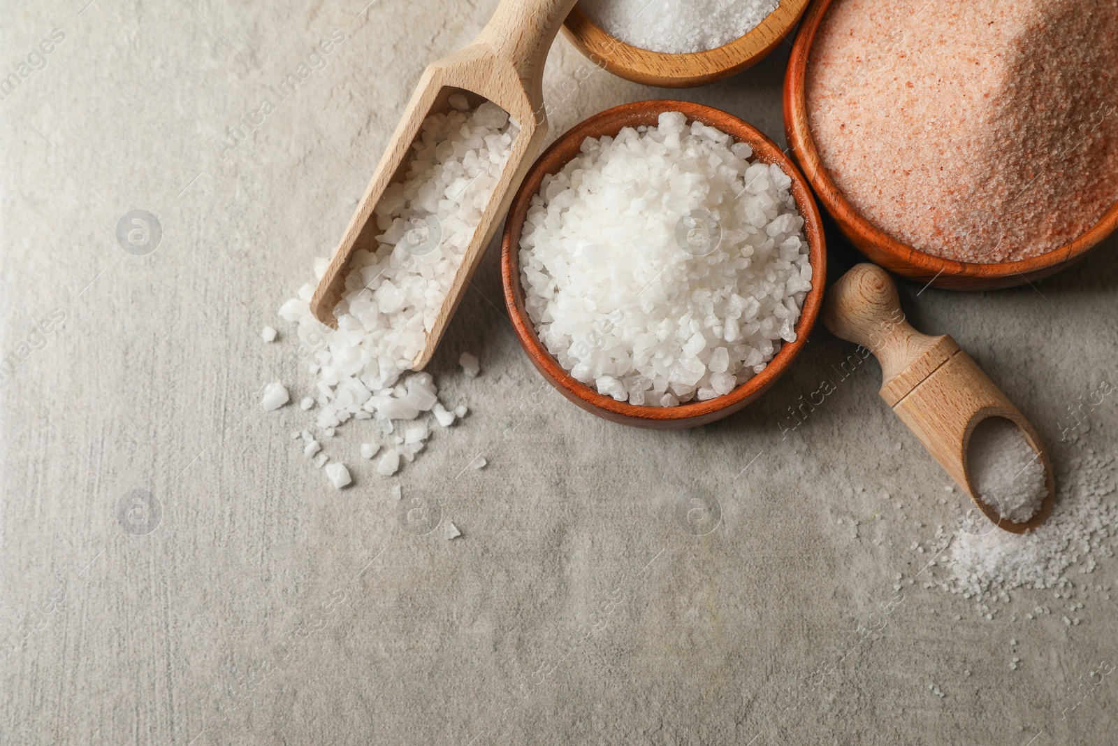 Photo of Different natural salt on grey textured table, flat lay. Space for text