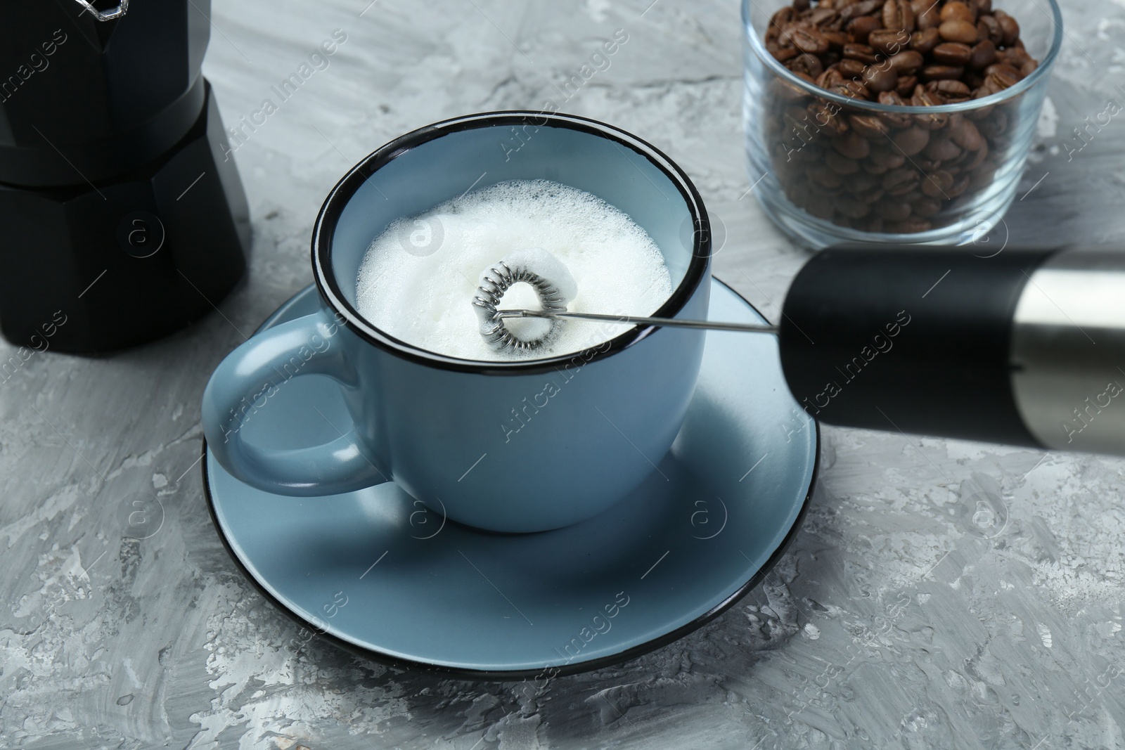 Photo of Whisking milk in cup with mini mixer (milk frother) on grey textured table, closeup