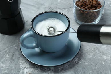 Photo of Whisking milk in cup with mini mixer (milk frother) on grey textured table, closeup