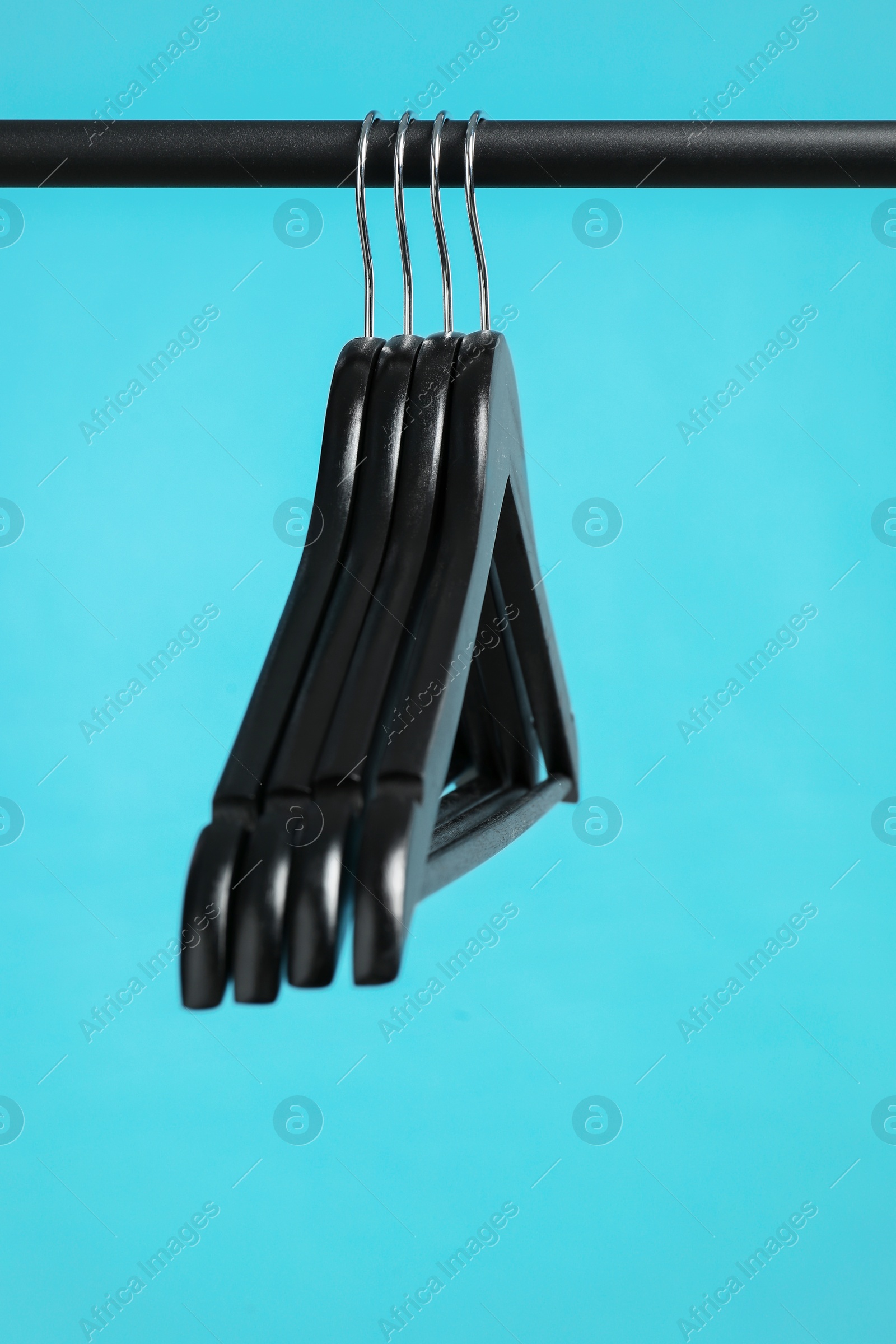 Photo of Black clothes hangers on rack against light blue background