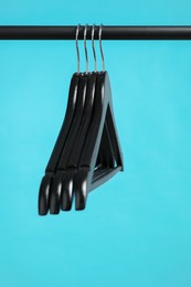 Photo of Black clothes hangers on rack against light blue background