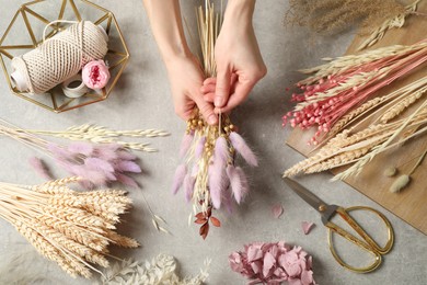 Photo of Florist making bouquet of dried flowers at grey stone table, top view