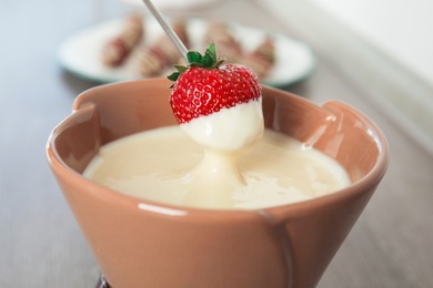 Ripe strawberry dipping into white chocolate fondue, closeup