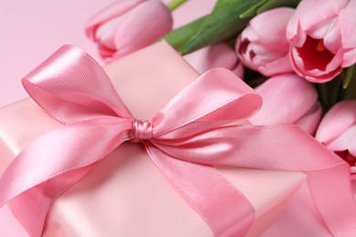 Beautiful gift box with bow and tulip flowers on pink background, closeup