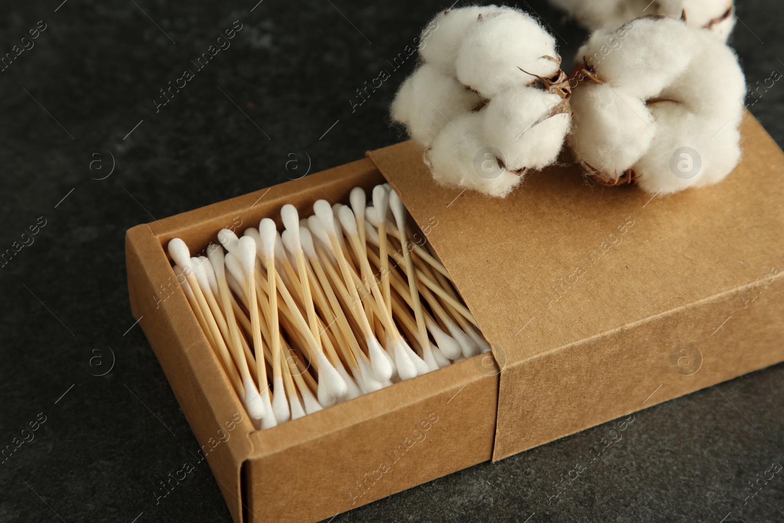 Photo of Cotton swabs and flowers on black table, closeup