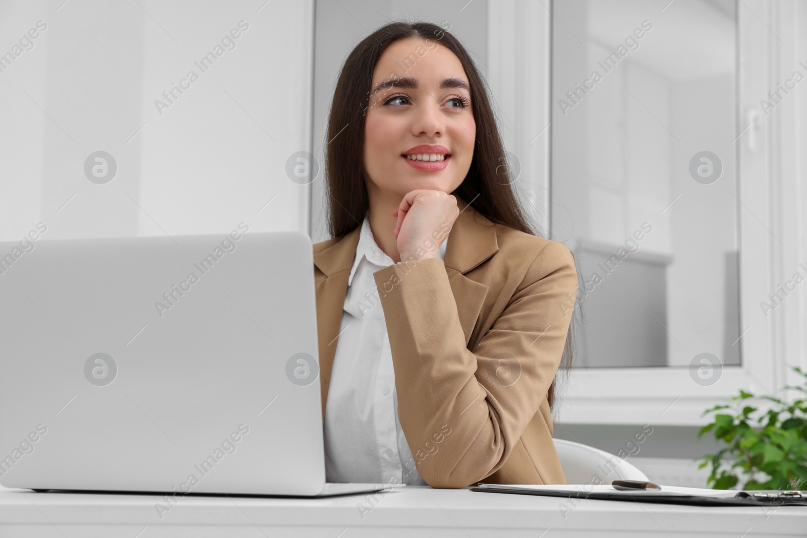 Photo of Young female intern working with laptop at table in office