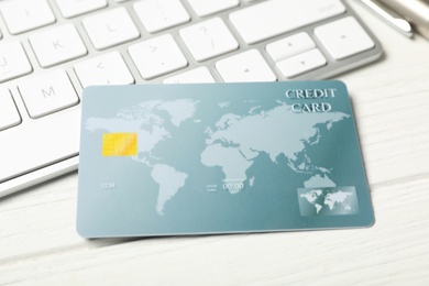Photo of Credit card near computer keyboard on white wooden table, closeup