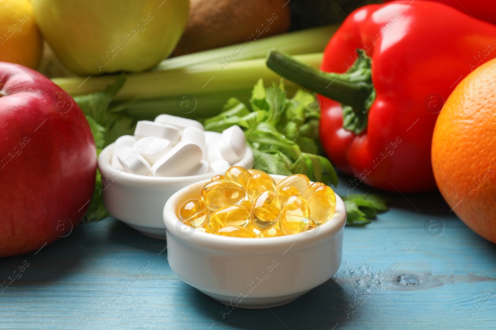 Photo of Dietary supplements. Bowls with different pills near food products on light blue wooden table, closeup