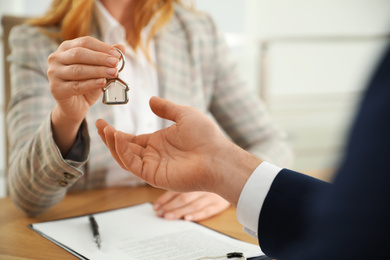 Photo of Real estate agent giving key with trinket to client in office, closeup