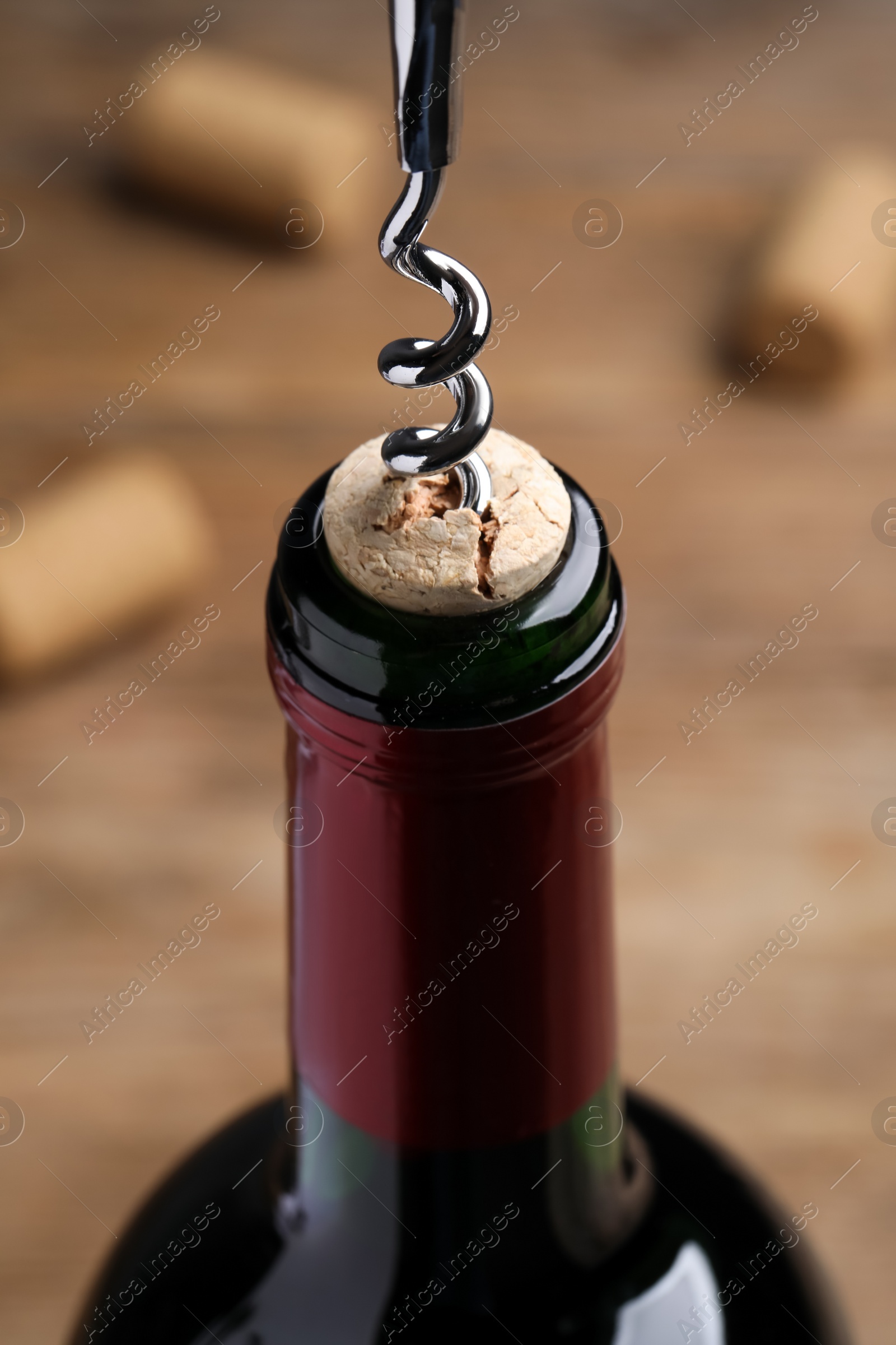Photo of Opening wine bottle with corkscrew on table, closeup