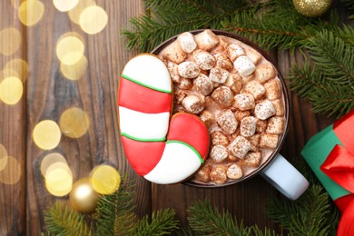 Photo of Tasty Christmas cookie in shape of candy cane, decor and cocoa with marshmallows on wooden table, flat lay. Space for text