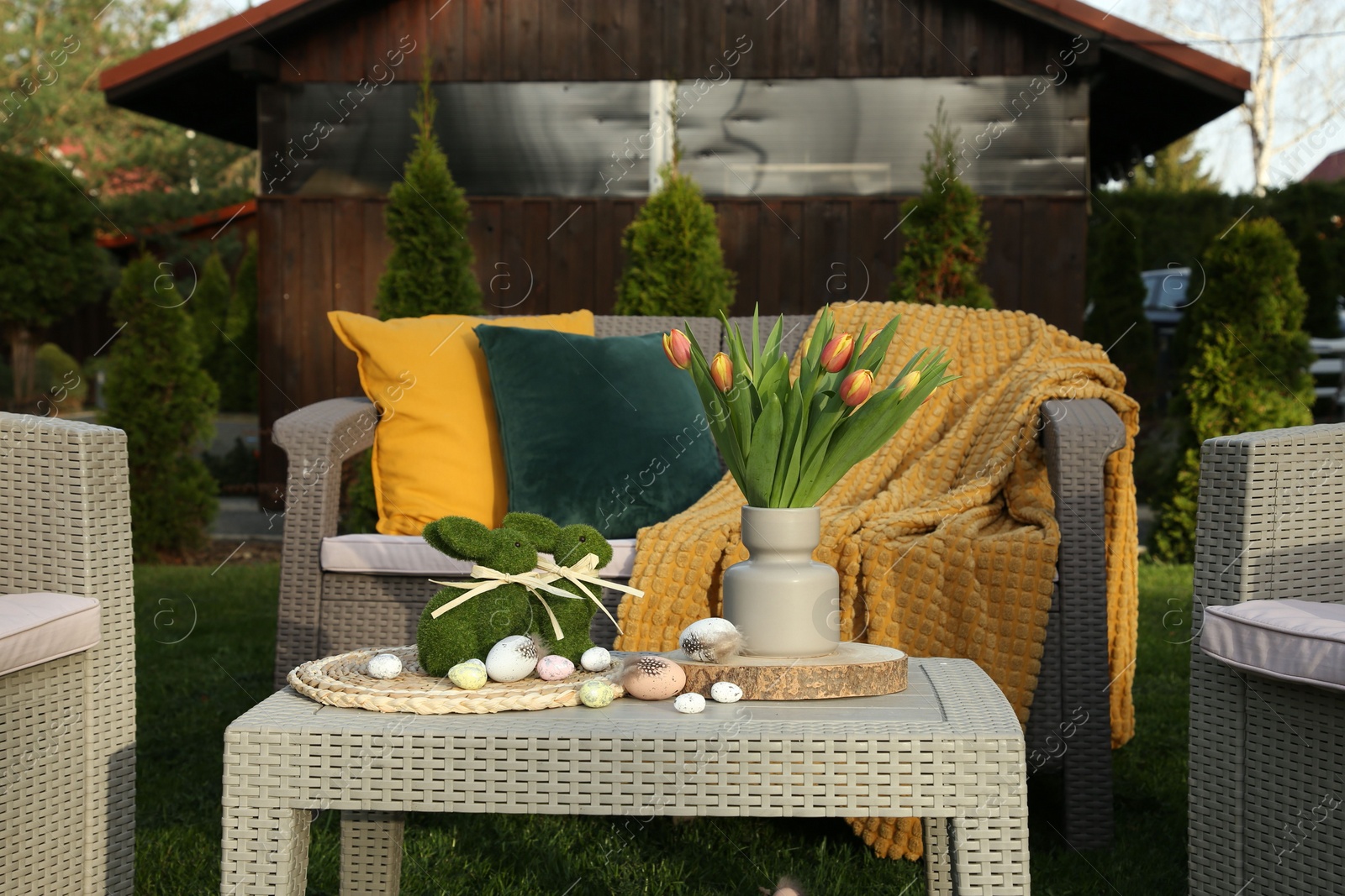 Photo of Terrace with Easter decorations. Bouquet of tulips in vase, bunny figures and decorative eggs on table outdoors