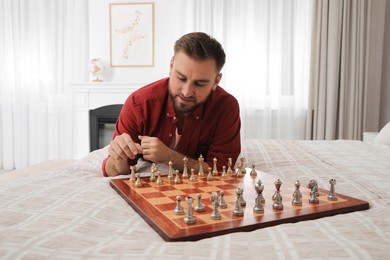 Photo of Young man playing chess alone on bed at home