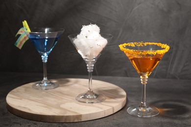 Photo of Tasty cotton candy cocktail and other alcoholic drinks in glasses on gray textured table
