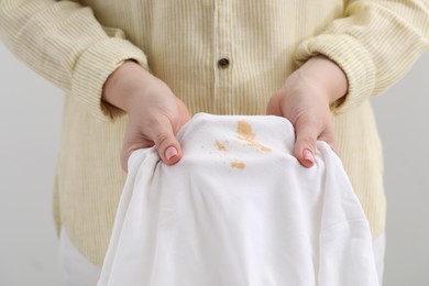 Woman holding shirt with stain against light background, closeup