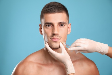 Photo of Man getting facial injection on light blue background. Cosmetic surgery