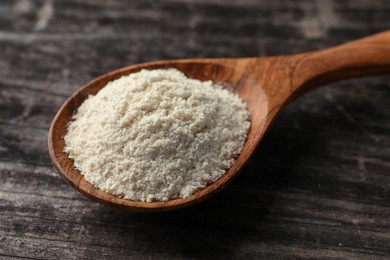 Photo of Spoon with quinoa flour on black wooden table, closeup