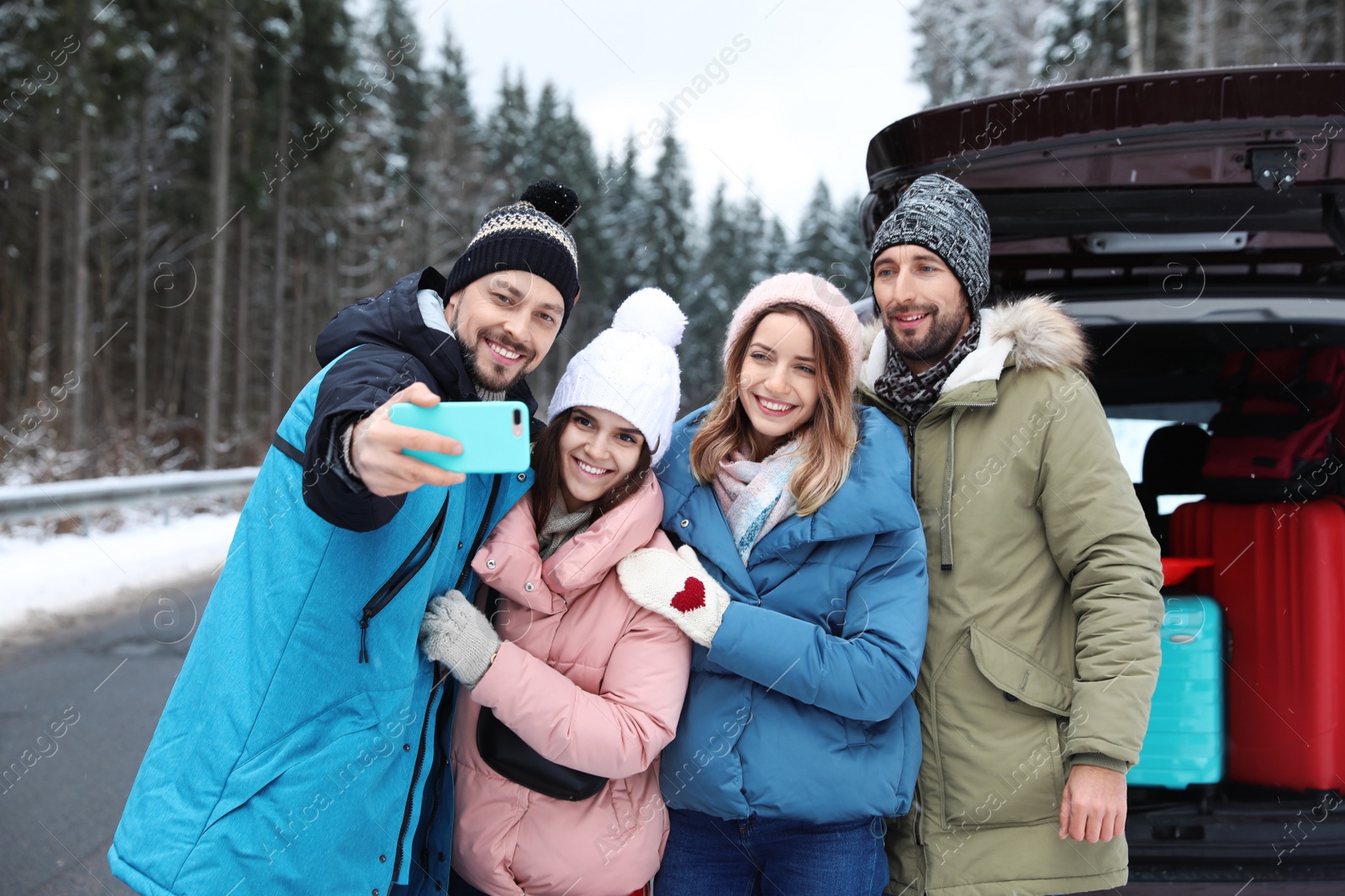 Photo of Friends taking selfie near open car trunk on road. Winter vacation