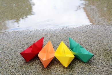 Photo of Beautiful colorful white paper boats on sandy beach near water outdoors