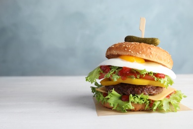 Photo of Tasty burger with fried egg on table against color background, space for text