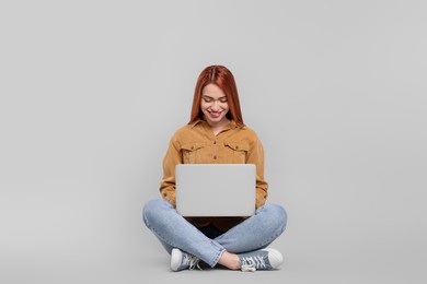 Photo of Smiling young woman working with laptop on grey background