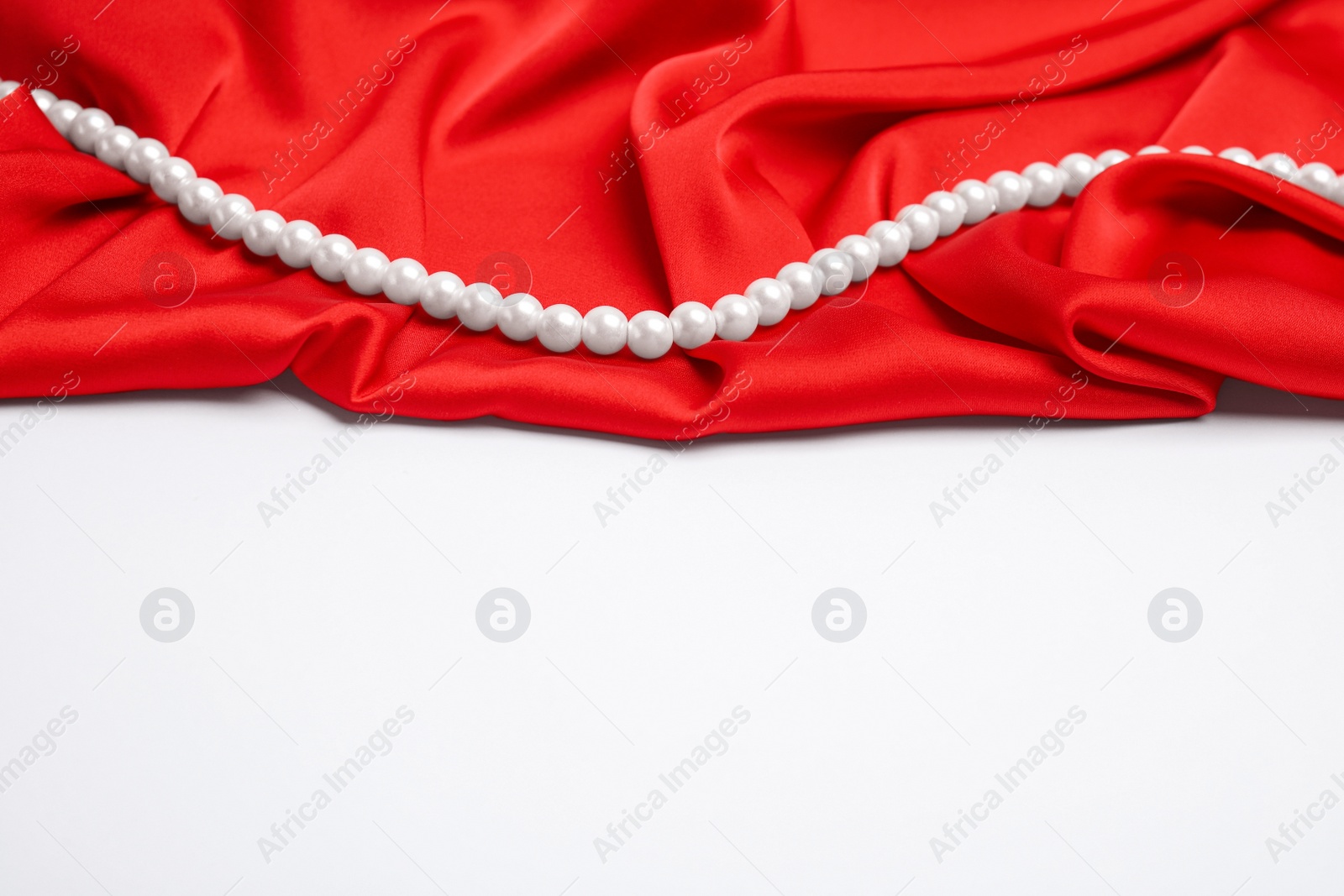 Photo of Beautiful pearls and red silk on white background