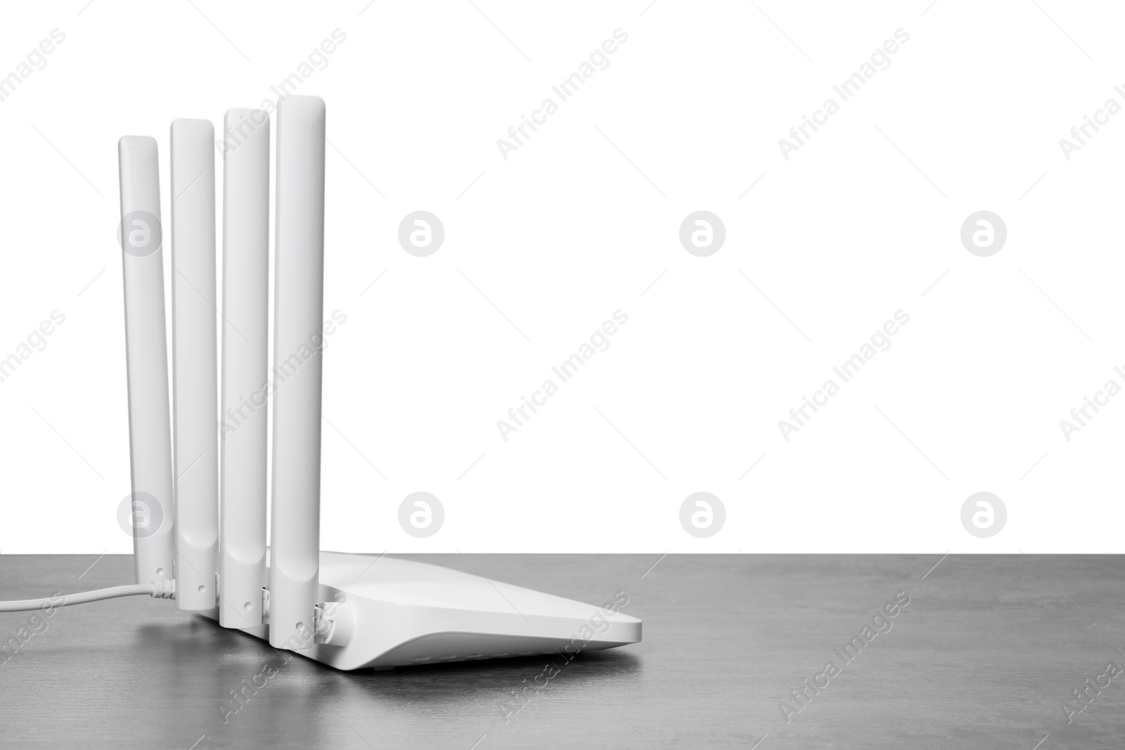 Photo of New modern Wi-Fi router on grey table against white background. Space for text