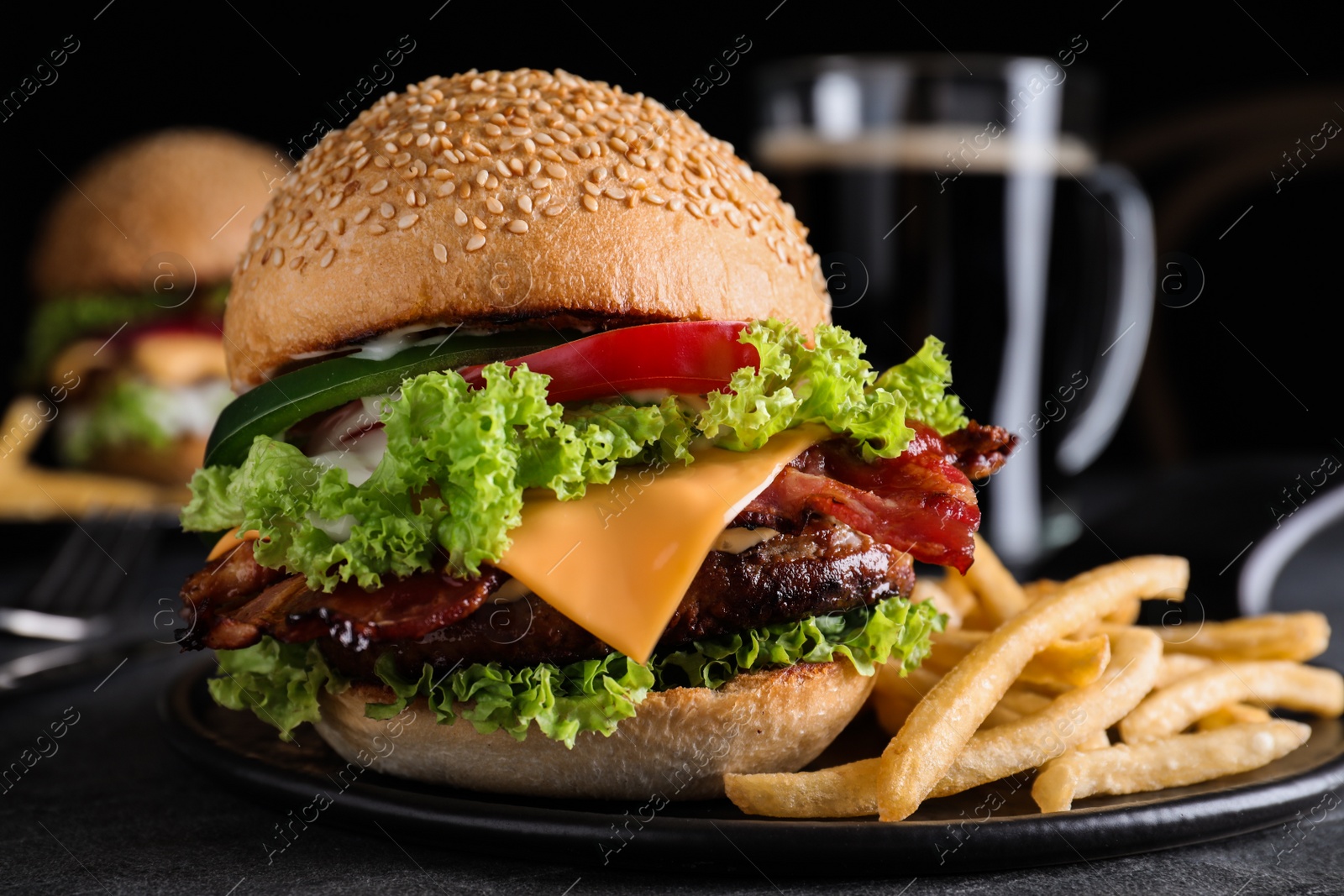 Photo of Fresh juicy bacon burger and fries on grey table, closeup